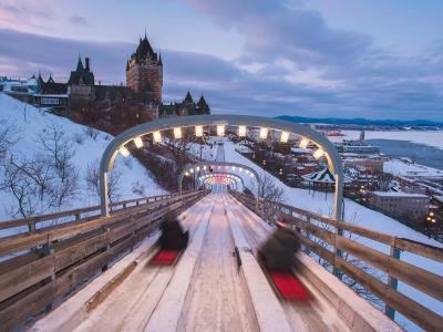 Two people slide on a tobogan at the Glissades de la Terrasse Dufferin, adjacent to the Fairmont Le Château Frontenac.