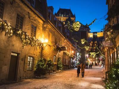 Un couple amoureux marche en soirée dans la rue du Petit-Champlain illuminée pour Noël et le temps des fêtes. 