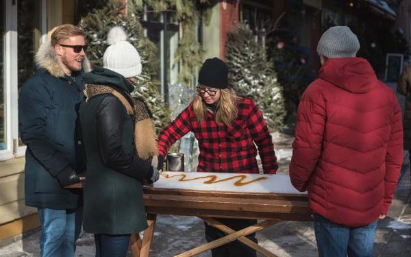 Trois passants s'arrêtent dans le quartier Petit-Champlain pour déguster de la tire sur neige dans une petite cabane à sucre.