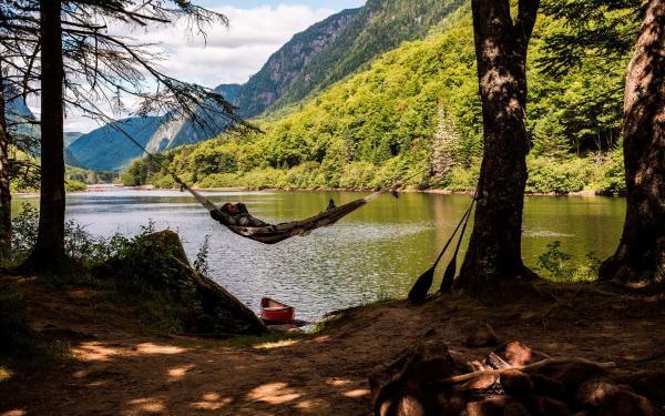 Un homme fait la sieste dans un hamac accroché aux arbres, sur le bord de la rivière, dans le Parc national de la Jacques-Cartier.