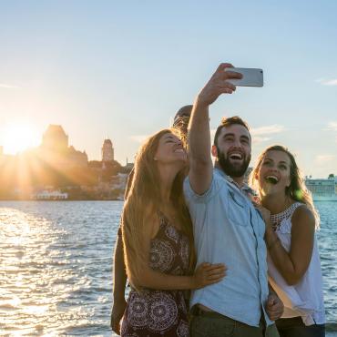 Friends take pictures of themselves at sunset, near the St.Lawrence River in Lévis with a panorama of Old Québec in the back.